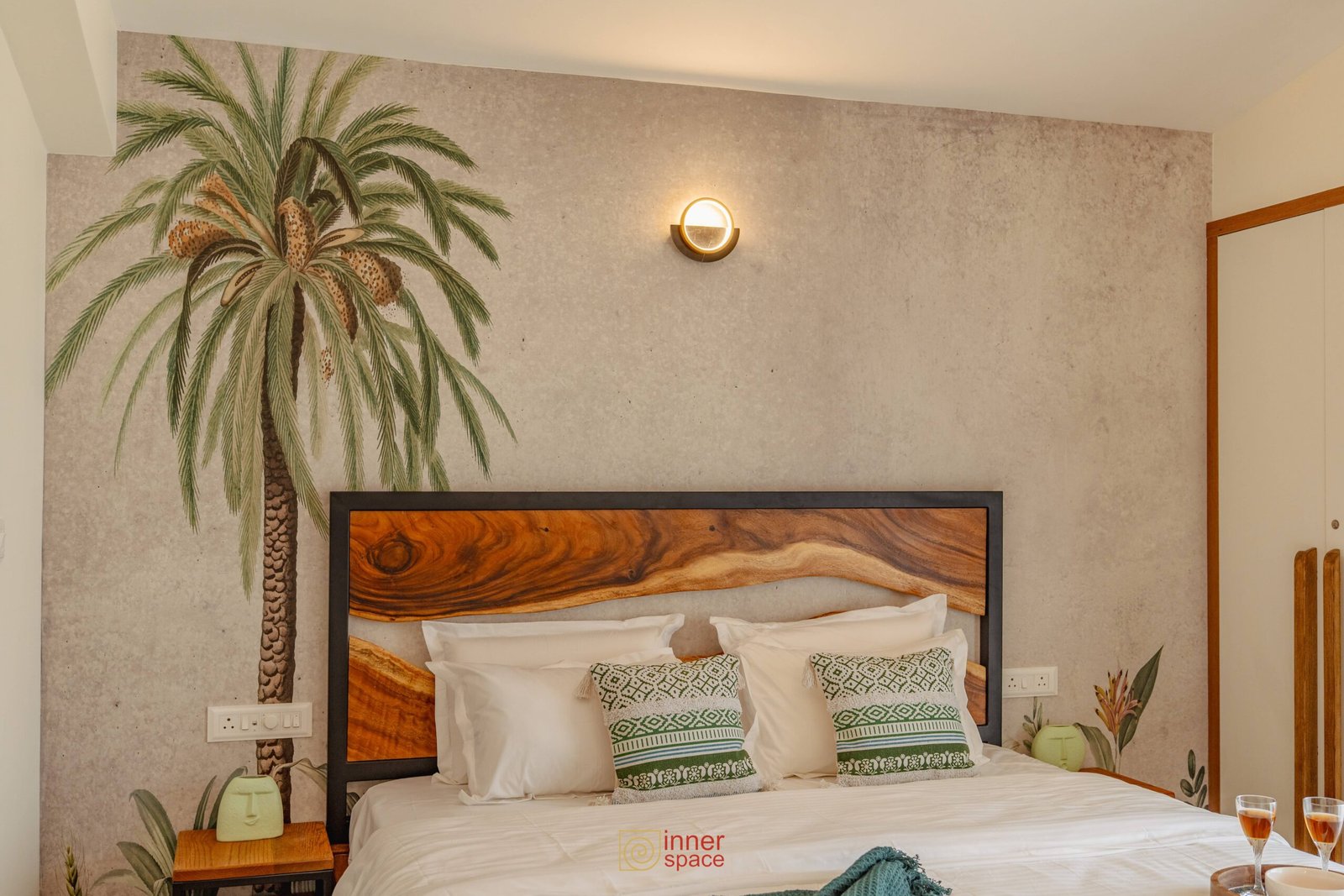 Bed with wooden headboard, white and green pillows in room with palm m